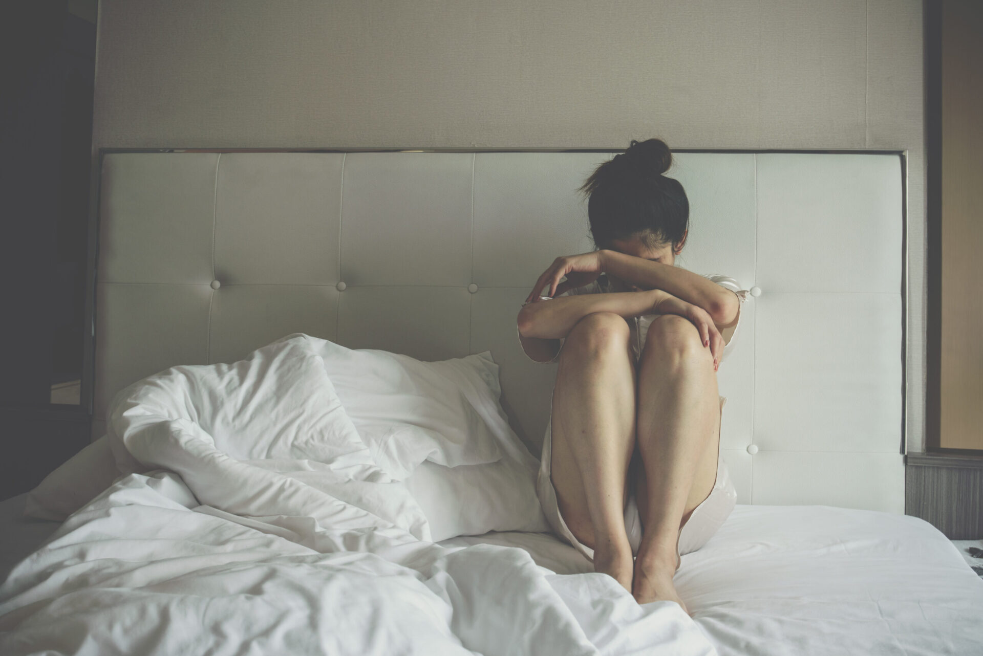 Portret przygnębionej kobiety siedzącej sama na łóżku w sypialni. Konceptualnie odzwierciedla złe samopoczucie związane z złamanym sercem, smutkiem i samotnością.
