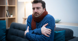 Mężczyzna czujący się bardzo zimno w domu pomimo noszenia ciepłych ubrań.