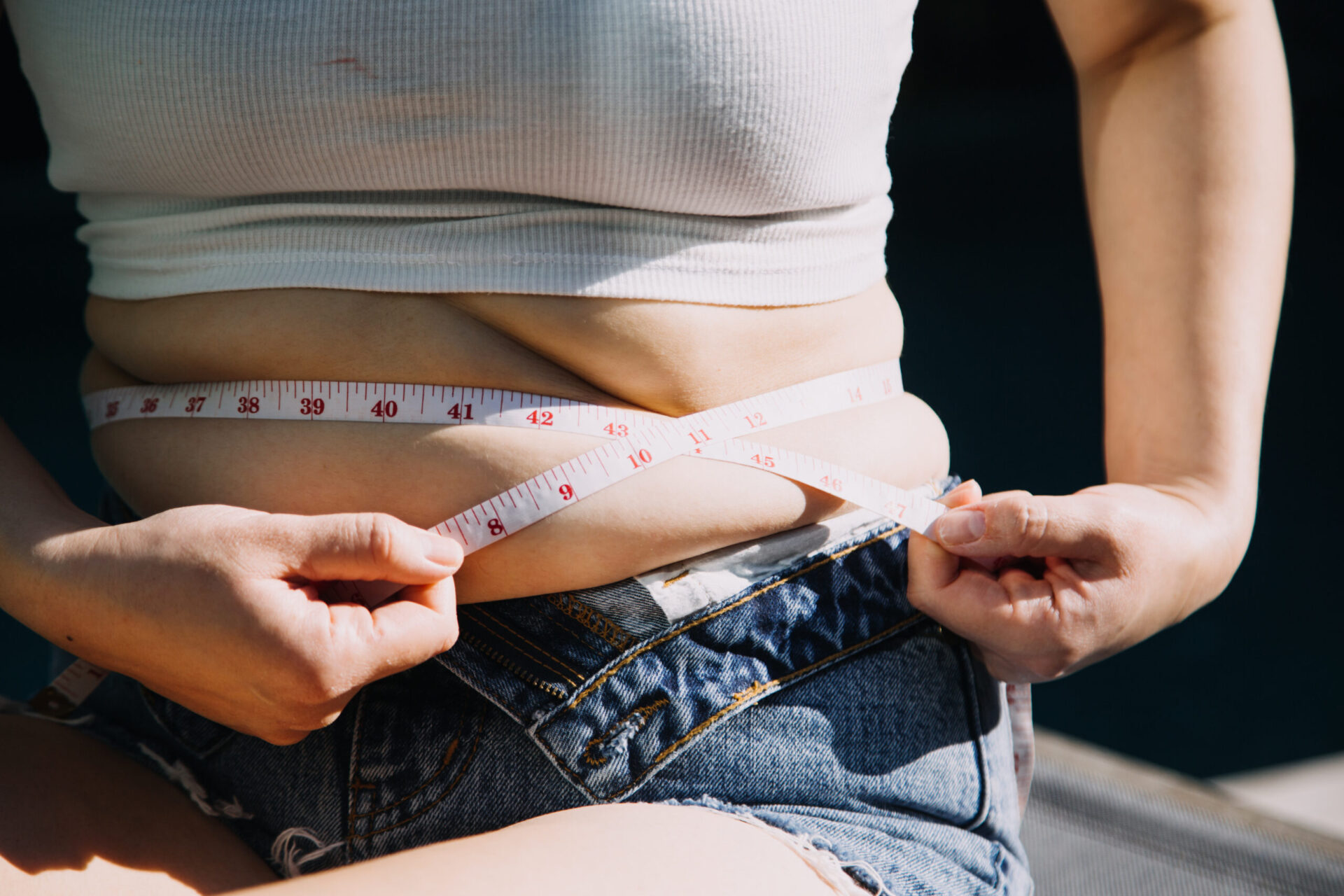 Gruba kobieta trzymająca nadmierną tkankę tłuszczową na brzuchu, przy użyciu miarki. Koncepcja diety i stylu życia w kontekście dbania o zdrowie.