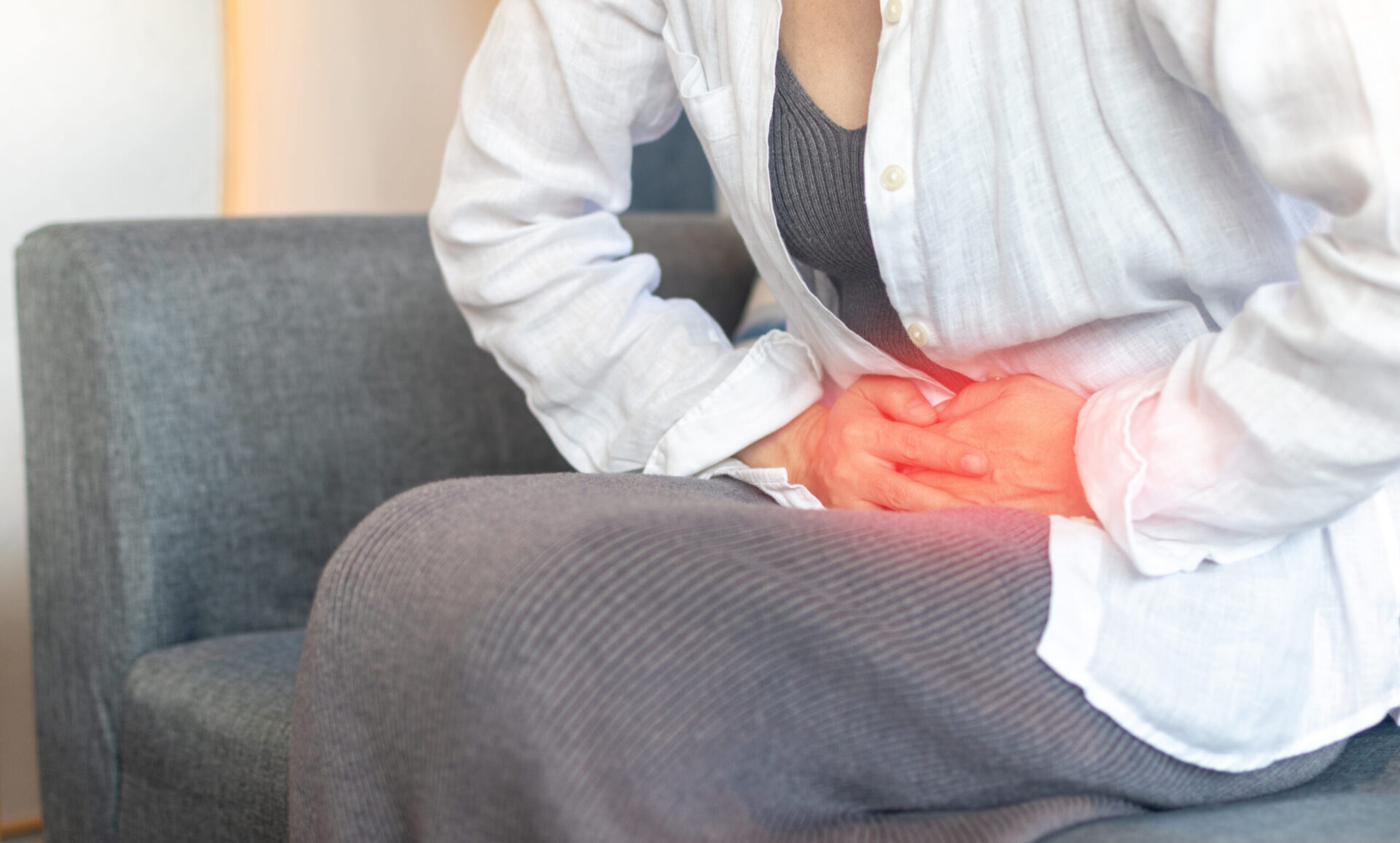 Ręce młodej kobiety na brzuchu jako oznaka bólu związana z bolesnymi miesiączkami, niestrawnością, problemami układu pokarmowego, biegunką lub chorobami układu rozrodczego u kobiet.