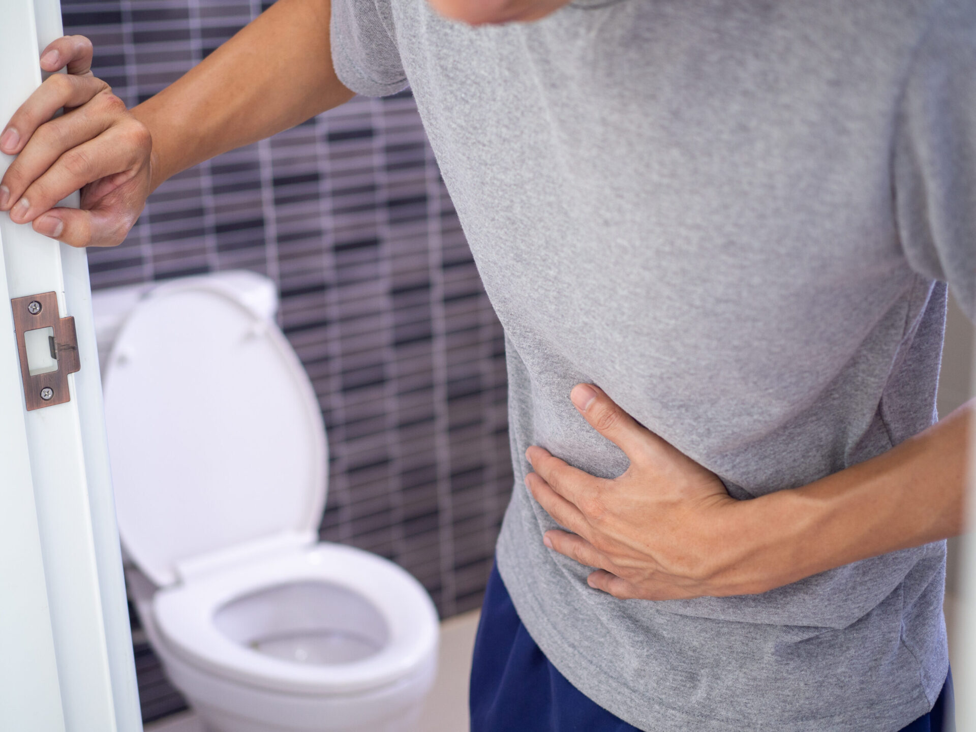 Mężczyźni stoją przed drzwiami łazienki, trzymając rękami brzuch z silnym bólem brzucha lub biegunką. Koncepcja skurczów żołądka i biegunki.